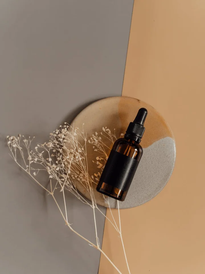 Amber glass serum dropper bottle on a geometric backdrop with dried flowers