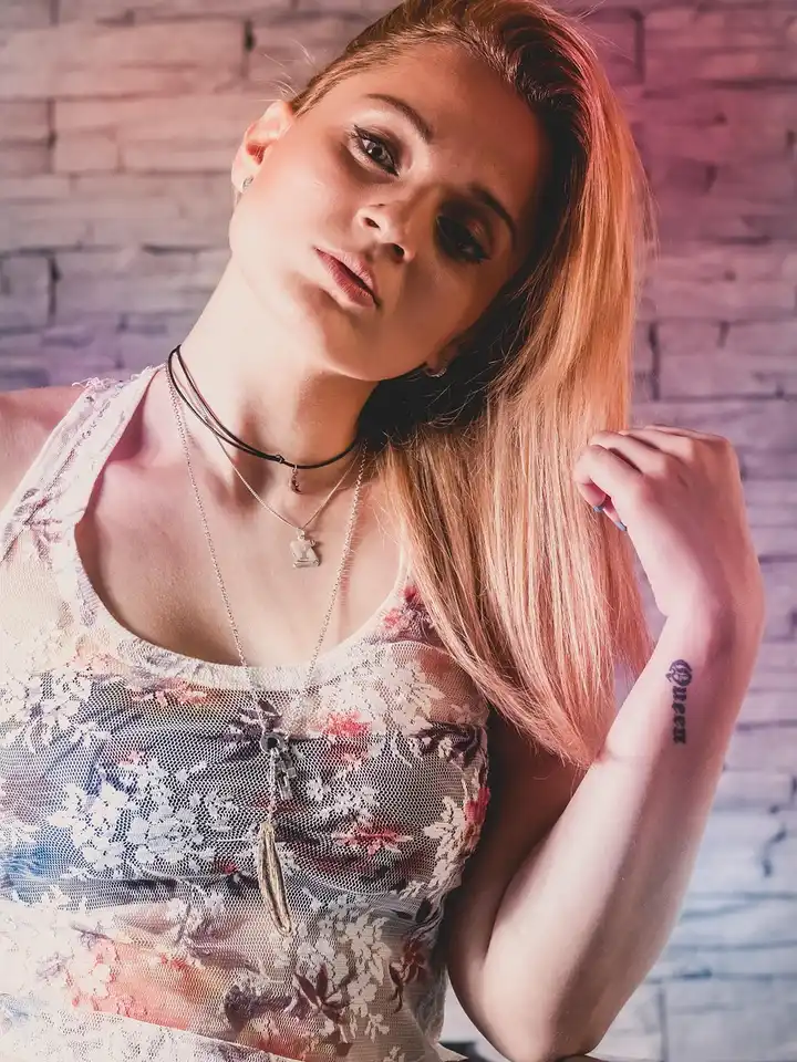 Person with long blonde hair wearing a floral top posing in front of a textured brick wall