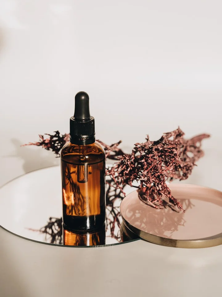 Amber glass dropper bottle on a round mirror with dried purple plant sprigs beside it