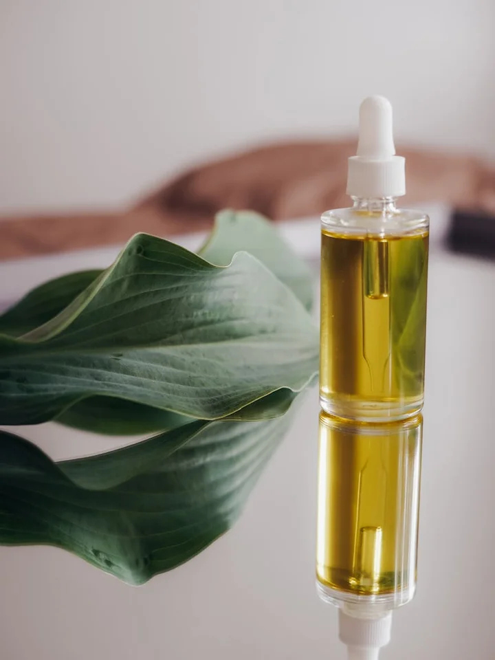 Close-up of a glass dropper bottle with golden serum beside a broad green leaf, representing nighttime skincare layering.