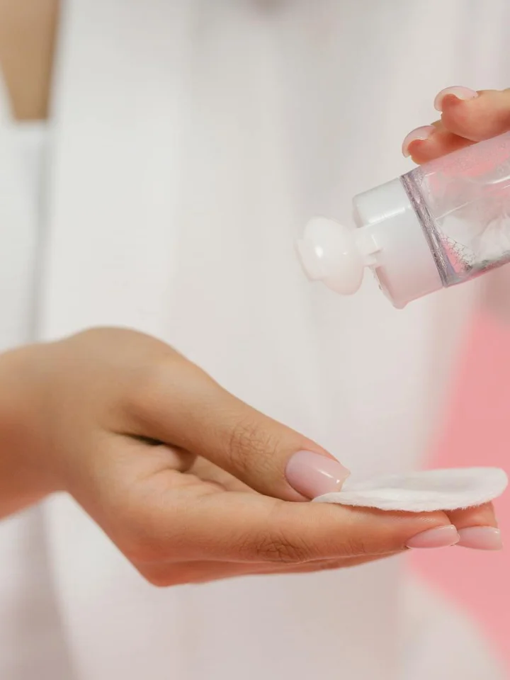 Close-up of a hand dispensing skincare product onto a cotton pad to apply non-comedogenic skincare
