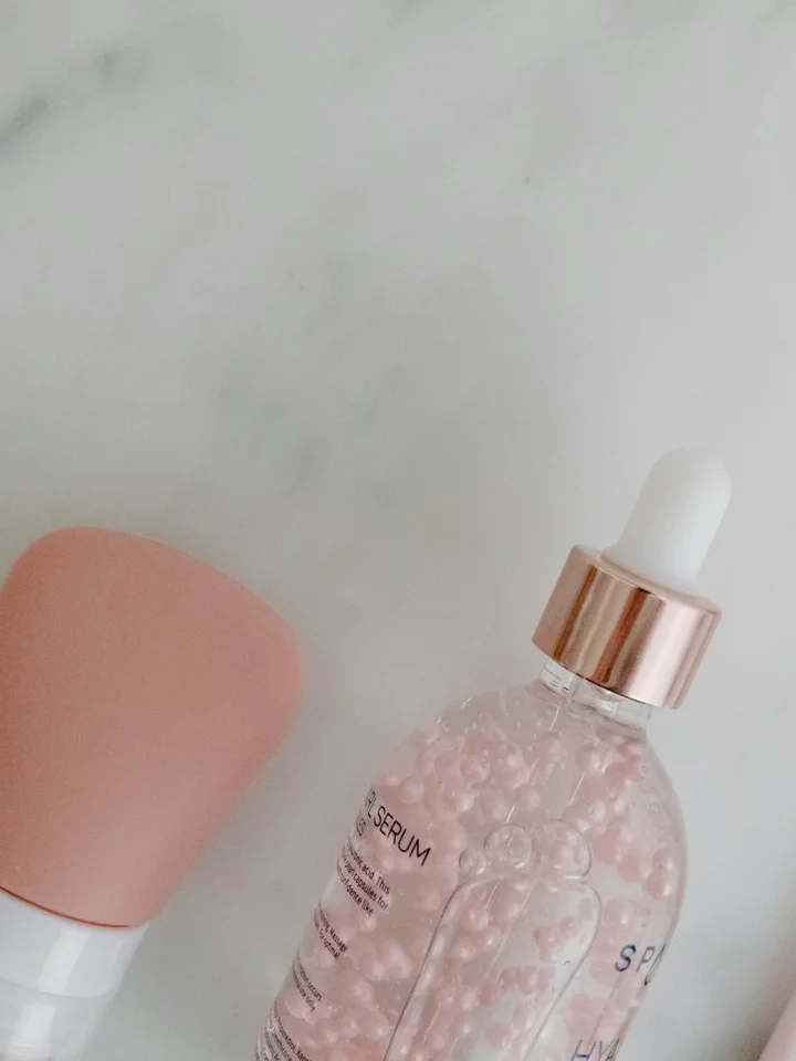 Close-up of a skincare serum bottle with a dropper and pink cap on a light marble surface