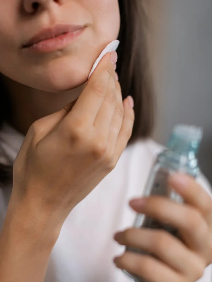 Close-up of a person applying skincare product with a cotton pad to their cheek