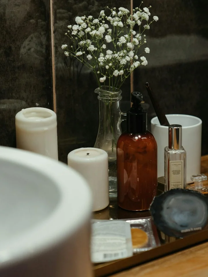 Skincare vanity with bottles, pumps, candles, and a small bouquet of baby's breath on a mirrored tray.