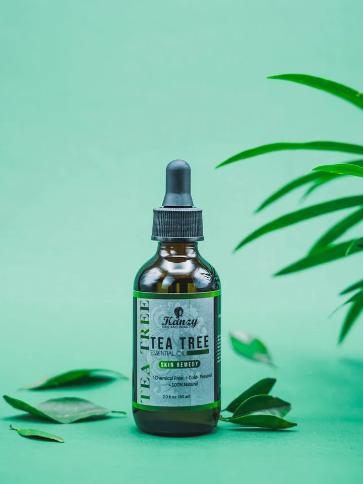 Dropper bottle labeled Tea Tree on a bright green background with scattered leaves