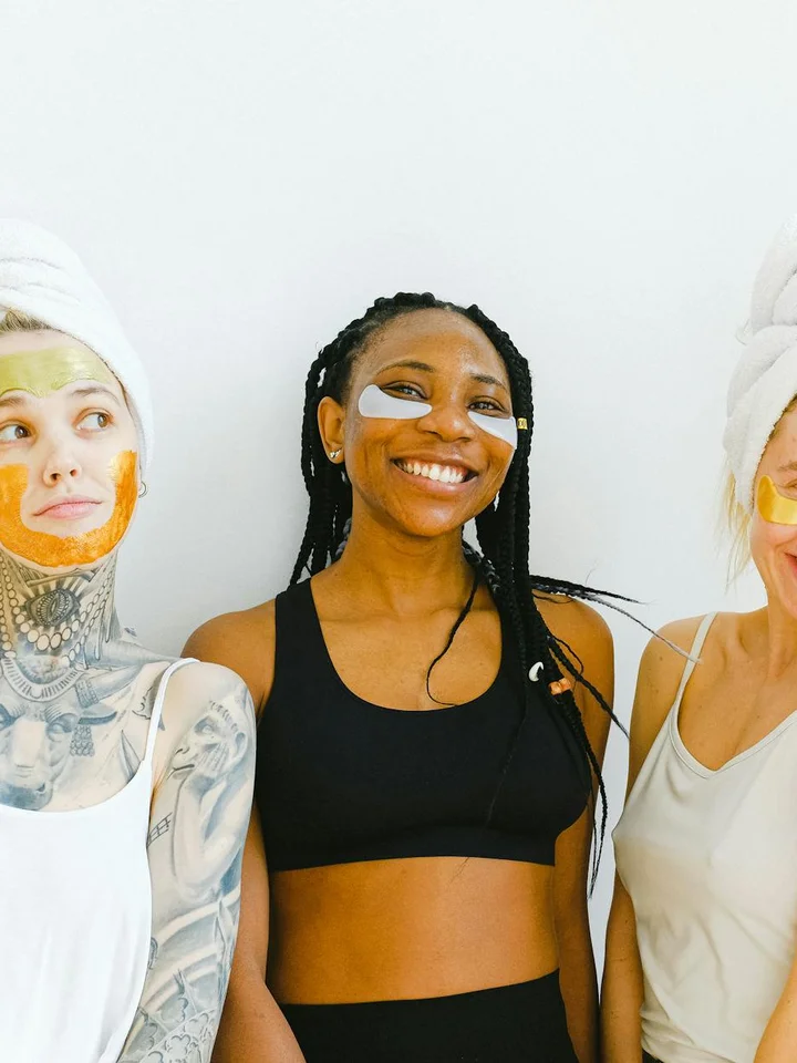 Three women wearing facial masks pose together in a bright, minimalist setting.
