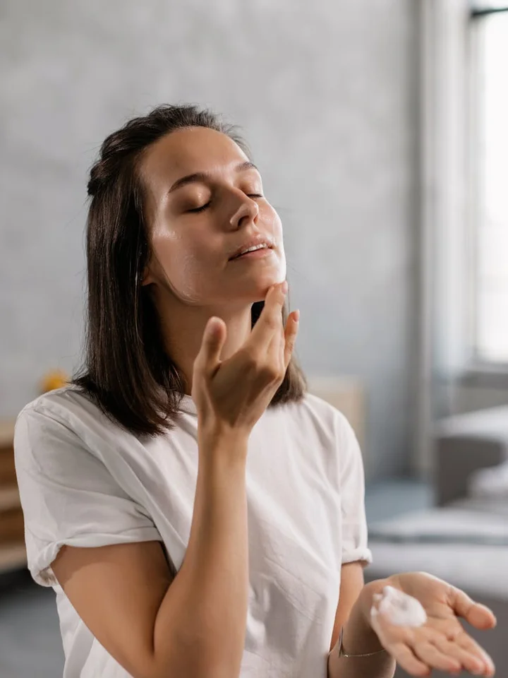 Woman with eyes closed gently touching her face during a skincare routine, illustrating cautious use of retinoids.
