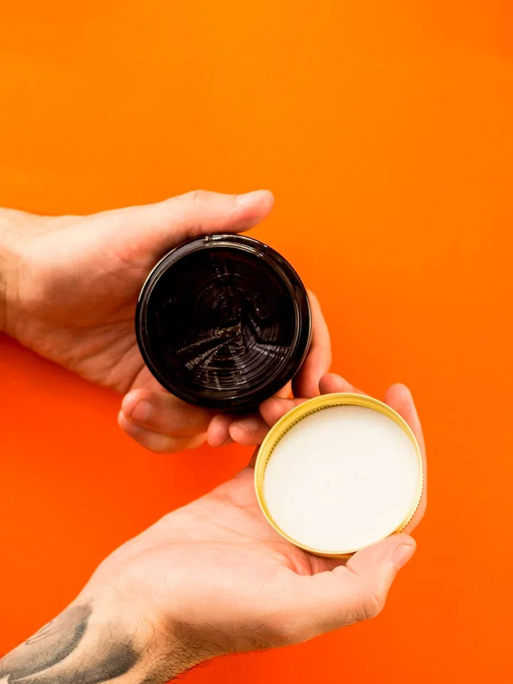 Hands holding an open jar of cream against an orange background, representing topical skincare treatments like tretinoin.
