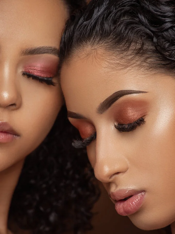 Close-up of two models with dewy, glass-skin makeup; pink-toned eyeshadow and flawless skin.