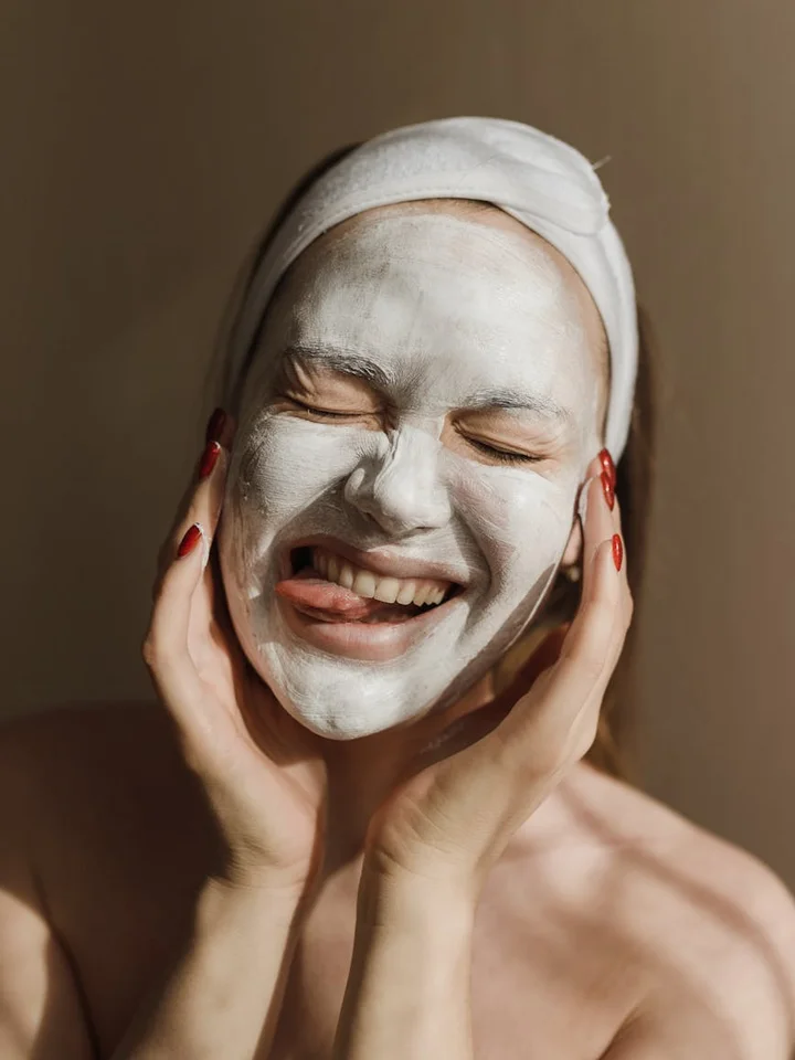 Model with a white facial mask and towel wrapped around the head, smiling.