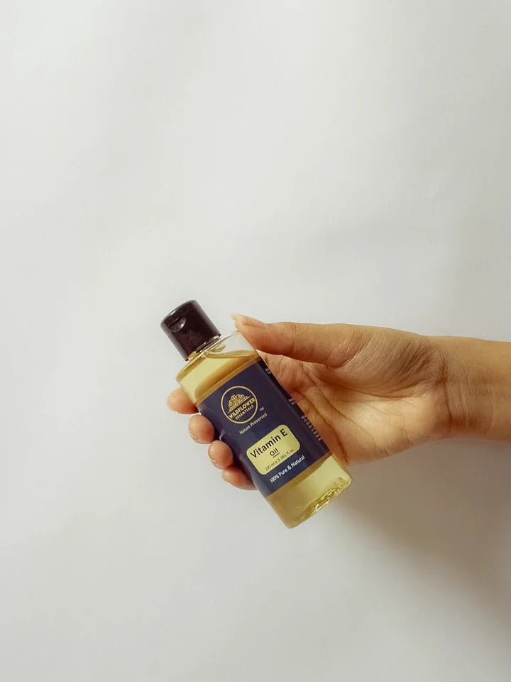 A hand holding a small bottle of Vitamin E oil against a plain white background.