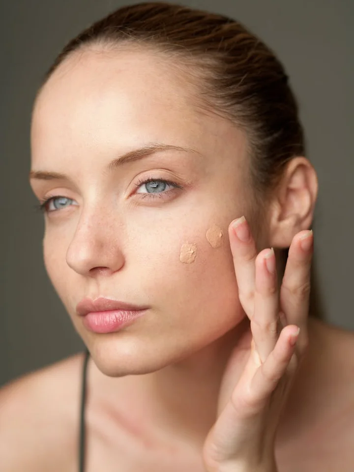 Close-up of a woman applying foundation to her cheek.