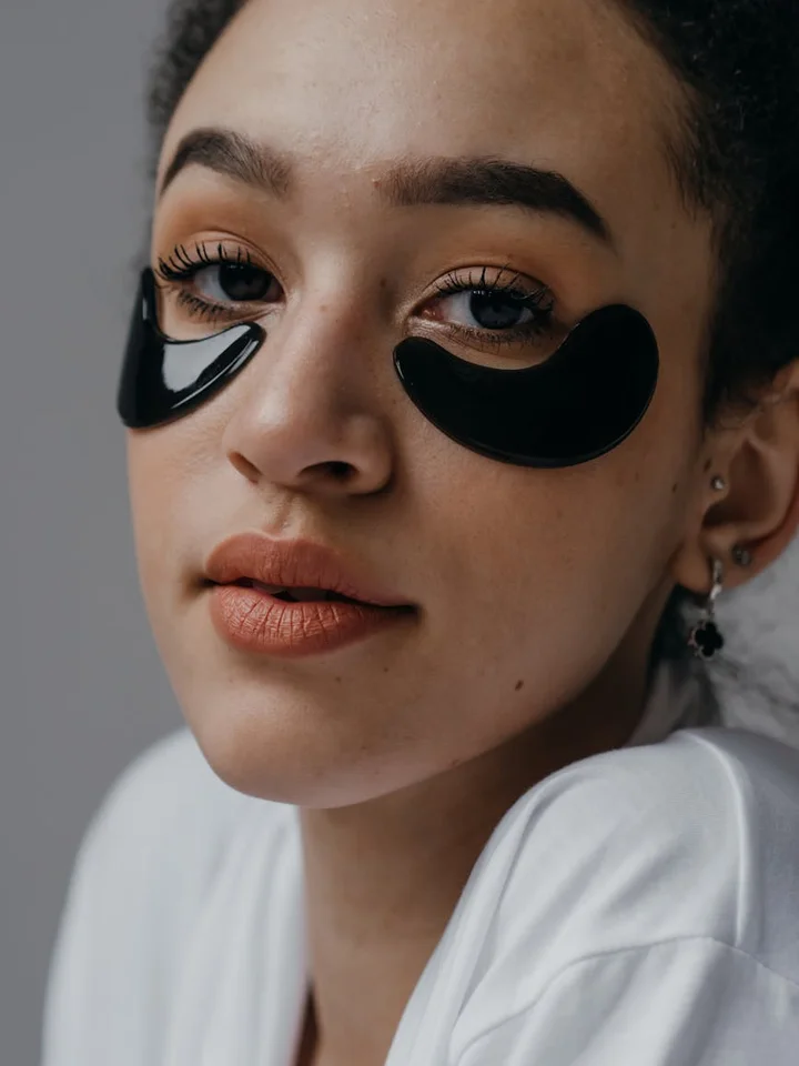 Close-up of a woman's face with black hydrogel under-eye patches.