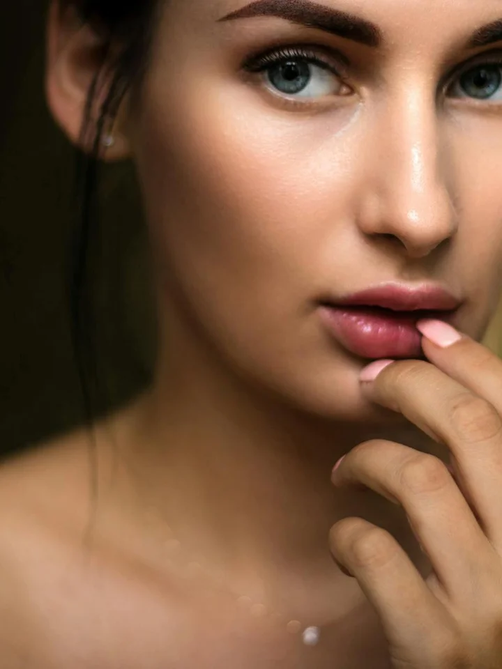 Close-up portrait of a woman with clear skin, gently touching her lips