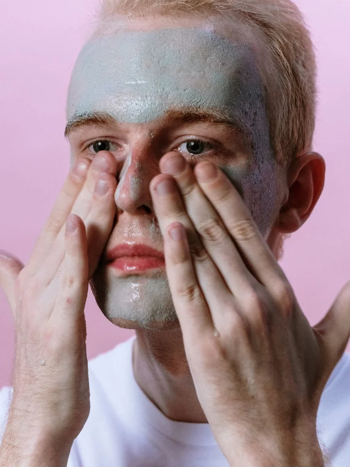 Person applying a blue-gray facial mask, hands on cheeks, close-up