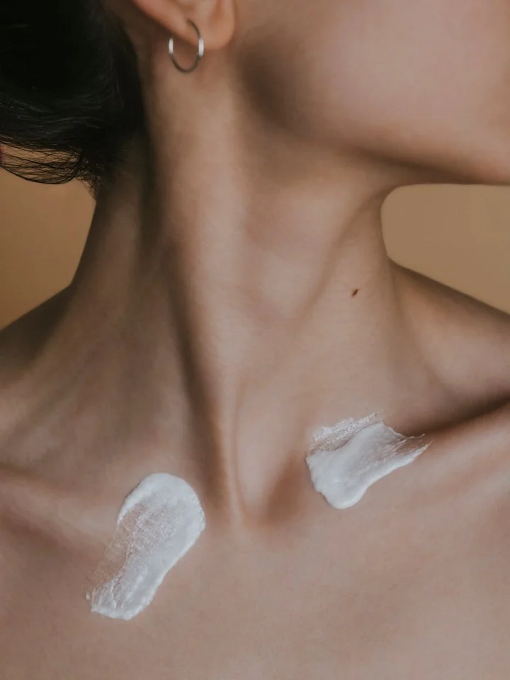 Close-up of a person's neck and shoulder with two patches of white topical cream applied to the skin.