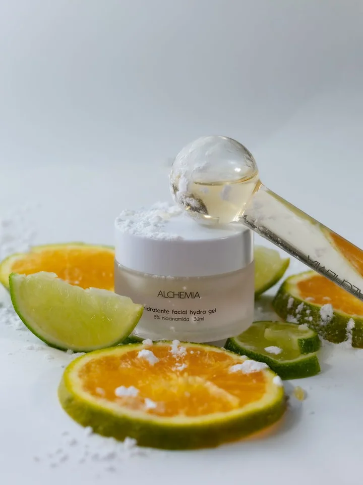 A small jar of skincare cream with a dropper, surrounded by slices of orange and lime with a light sprinkle of salt on a white surface.