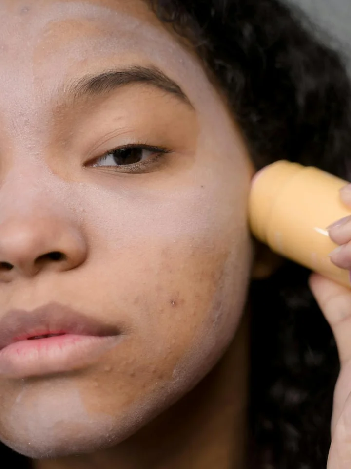 Close-up of a person applying a skincare product to the cheek with a small roll-on applicator