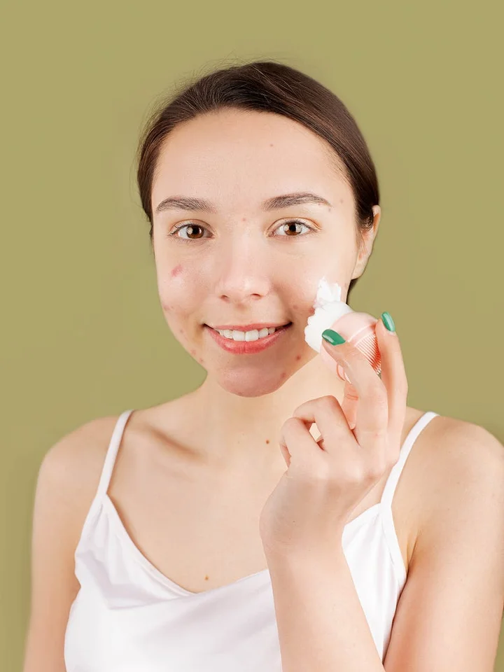Smiling woman applying skincare product to her face with a cotton pad.