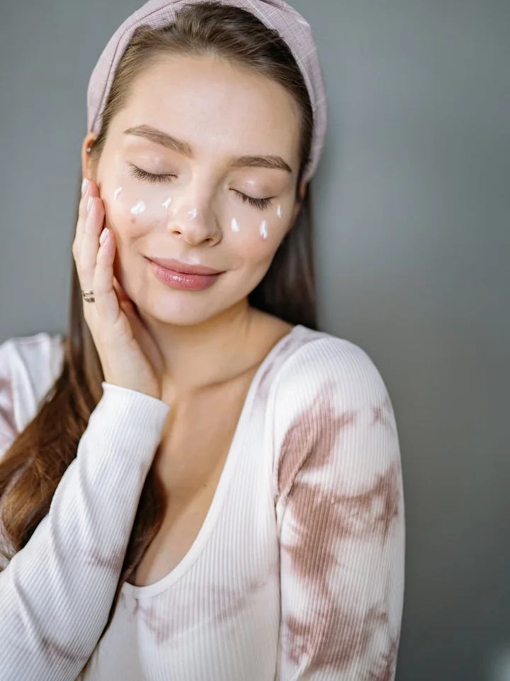 Young woman with a headband applying skincare cream to her face, illustrating topical retinoid treatment.