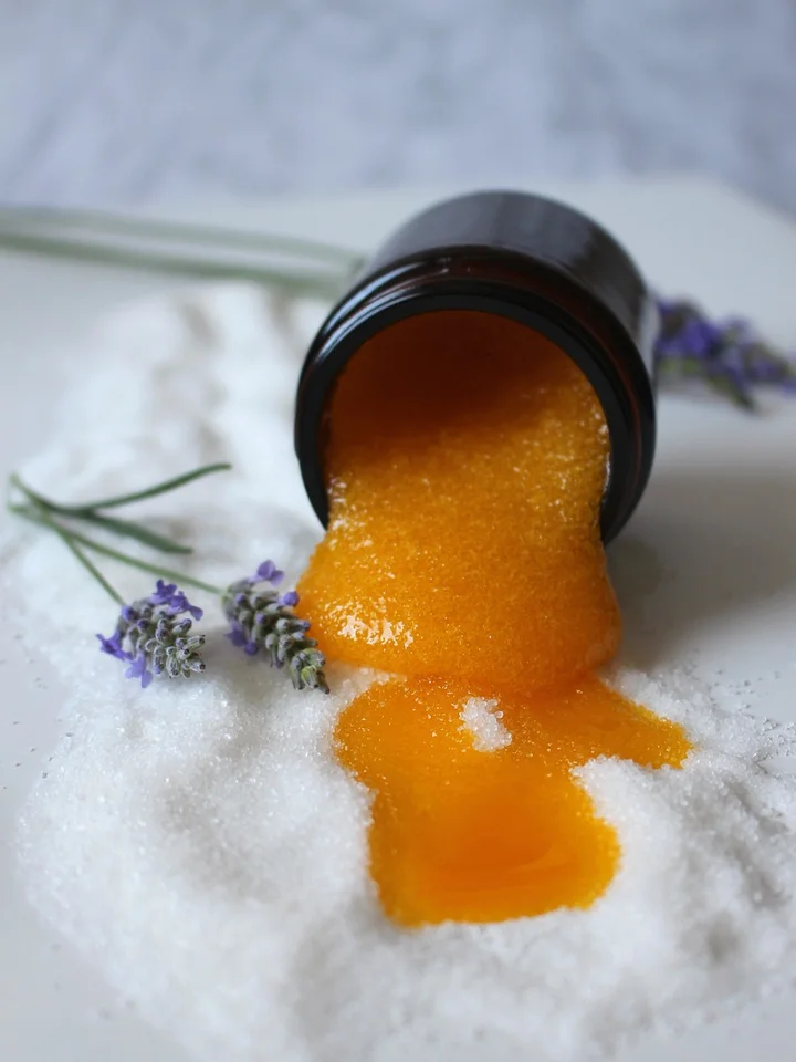 Orange gel-like extract pouring from a dark bottle onto a white surface with lavender sprigs.
