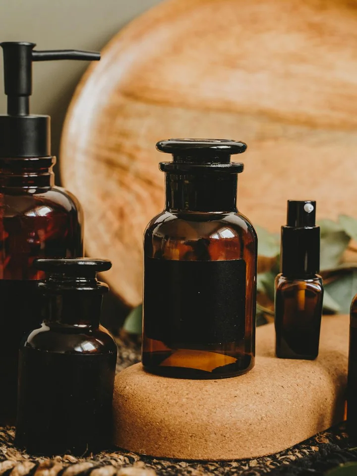 Amber glass skincare bottles with pumps and droppers arranged on a cork surface against a wooden backdrop.