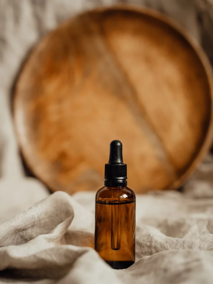 Amber glass dropper bottle resting on light fabric with a blurred wooden backdrop.