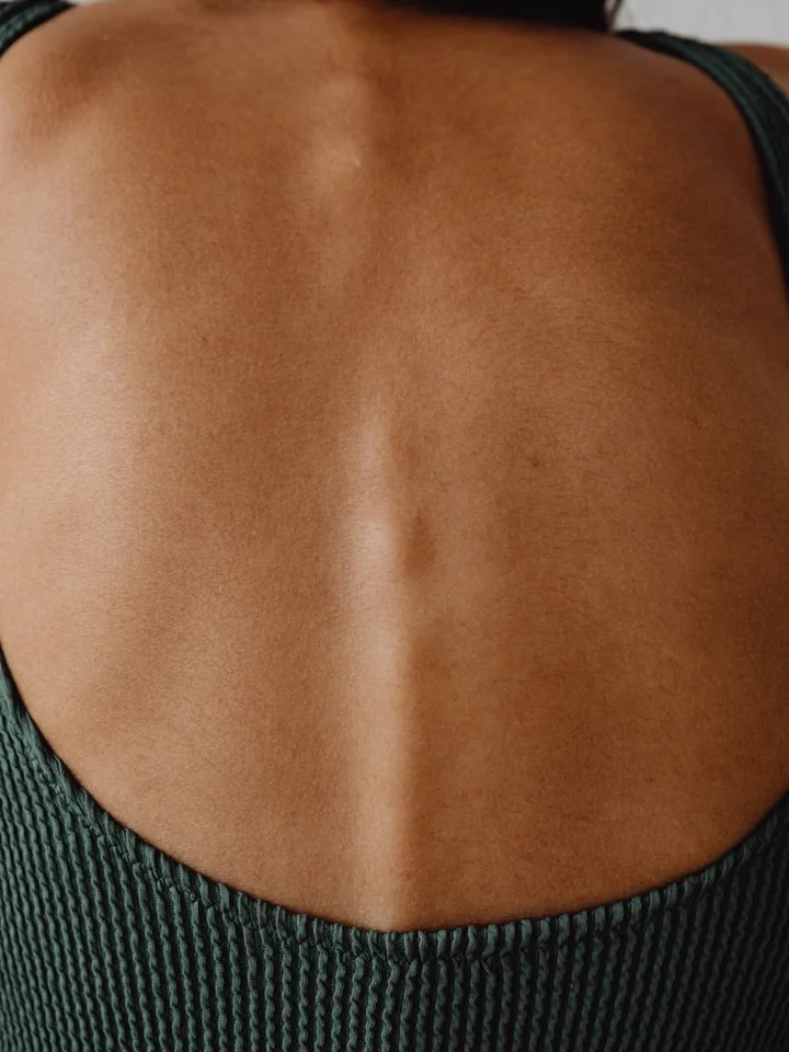 Close-up of a person’s upper back with a visible vertical line along the spine and smooth surrounding skin, illustrating skin texture and fine lines.