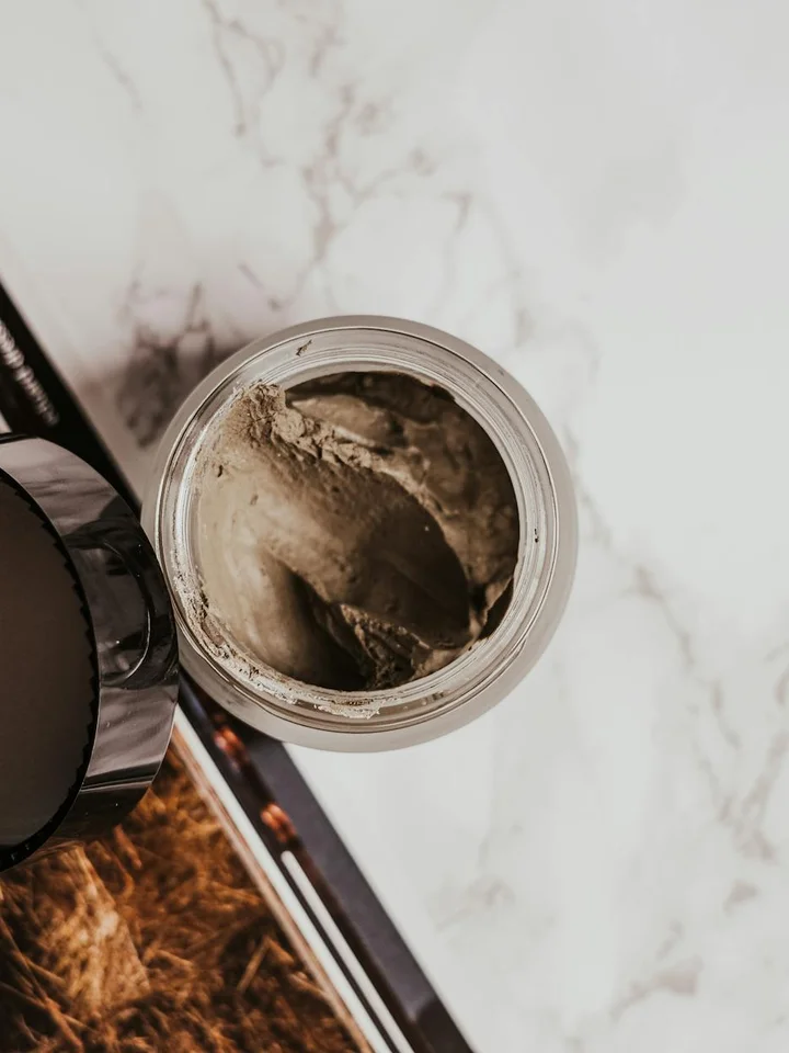Open jar of cream placed on a marble surface with a dark lid nearby, illustrating skincare ingredient screening for acne-prone skin.
