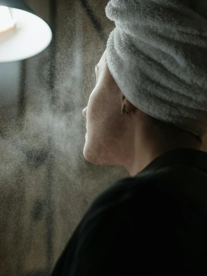 Close-up of a person with a towel wrapped around their head, steam rising in a spa-like setting.