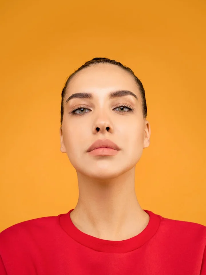 Portrait of a young woman with a neutral expression against an orange background.