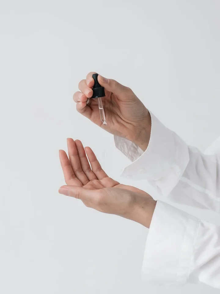 Hands in a white lab coat using a dropper to dispense liquid onto the palm