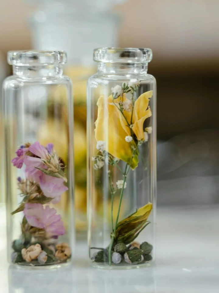 Two clear glass bottles containing dried flowers with a blurred background.