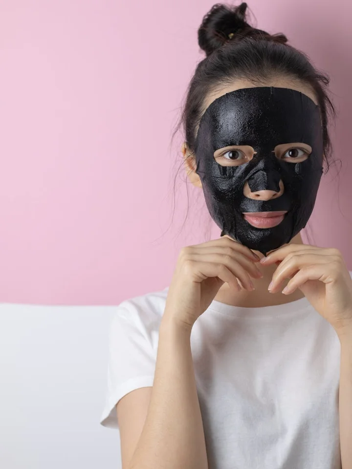 Person wearing a dark facial mask against a pink background