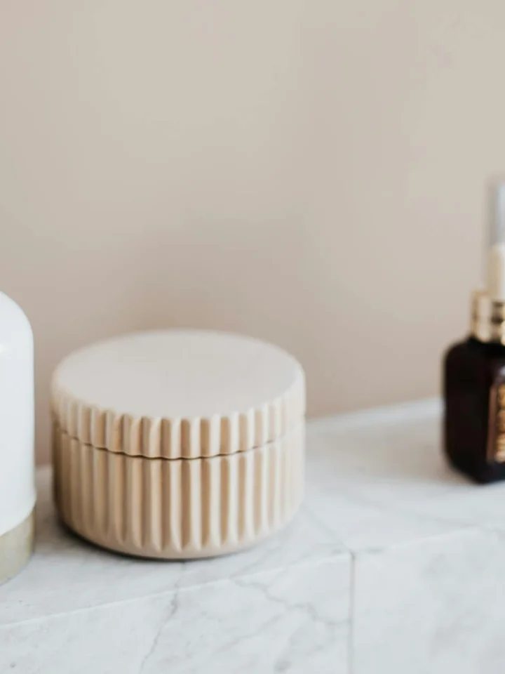 Close-up photo of skincare containers on a marble surface, featuring a beige ribbed cream jar and two dark bottles