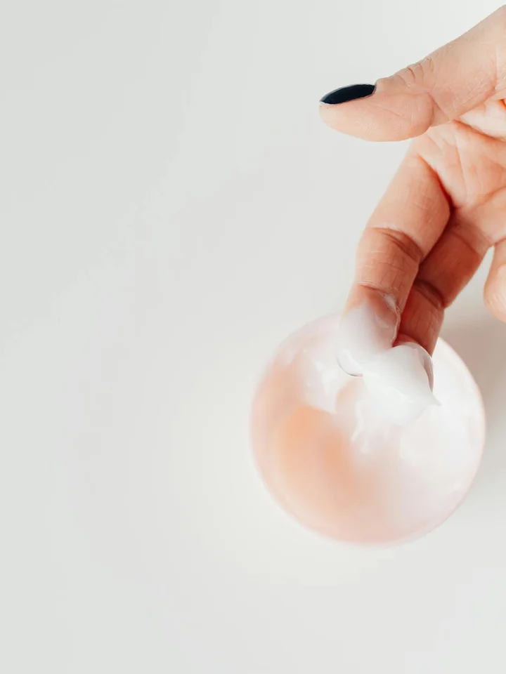 Close-up of a hand holding a small dollop of white cream on the fingertip