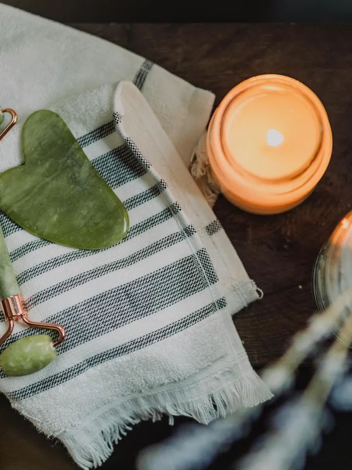 Daily skincare setup featuring a green gua sha tool on a striped towel and a lit candle, symbolizing routine skin barrier care.