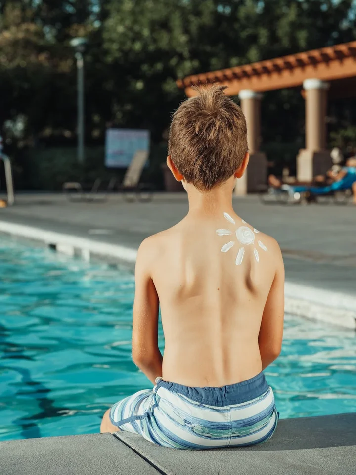 Back view of a child sitting at the pool edge with a sun-shaped sunscreen design on their upper back.