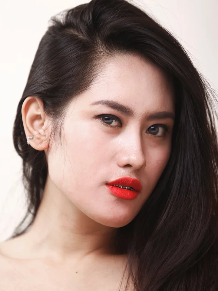 Close-up portrait of a woman with dark hair and bright red lipstick, showcasing makeup suitable for acne-prone skin.