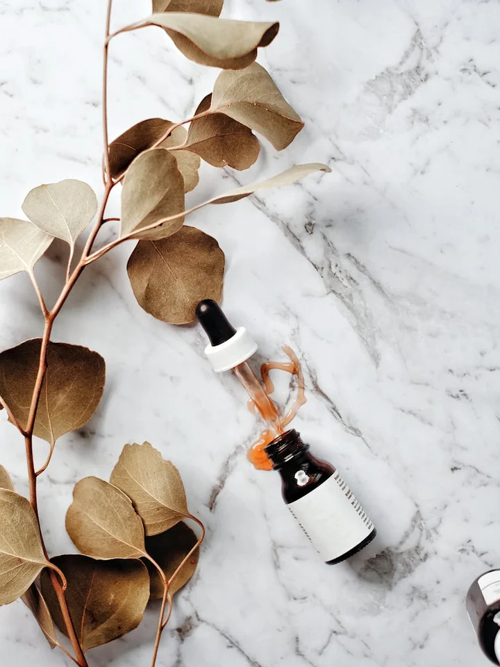 Skincare serum dropper bottle on a white marble surface with dried eucalyptus leaves nearby.
