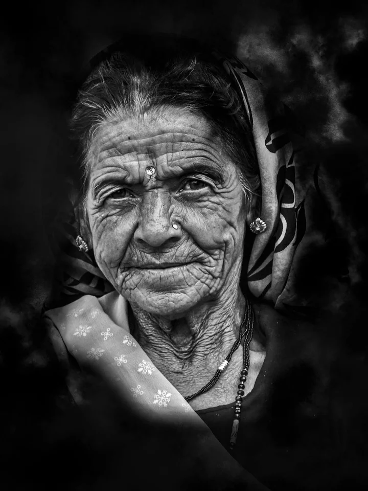 Black-and-white portrait of an elderly woman wearing a patterned headscarf, with a calm, weathered face and subtle wrinkles.