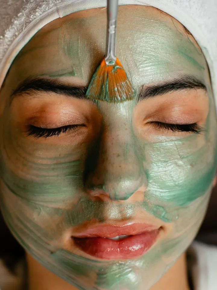 Close-up of a person with a green facial mask being applied with a brush
