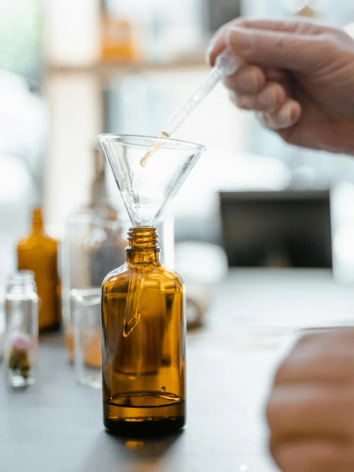 Laboratory scene showing a dropper releasing oil into an amber glass bottle, highlighting handling of oil-based botanical extracts to prevent oxidation.
