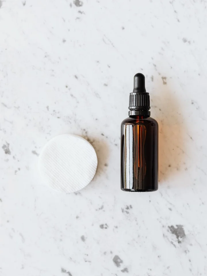 Brown glass dropper bottle and a white cotton pad on a light marble surface, symbolizing professional skincare evaluations.