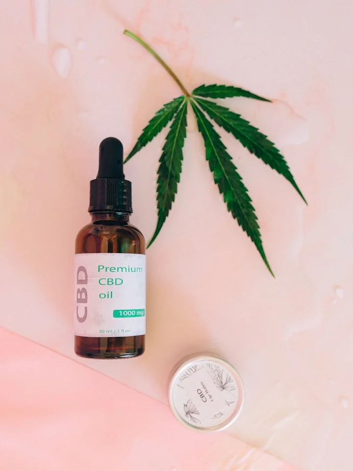 CBD oil bottle with dropper and a cannabis leaf on a pink background