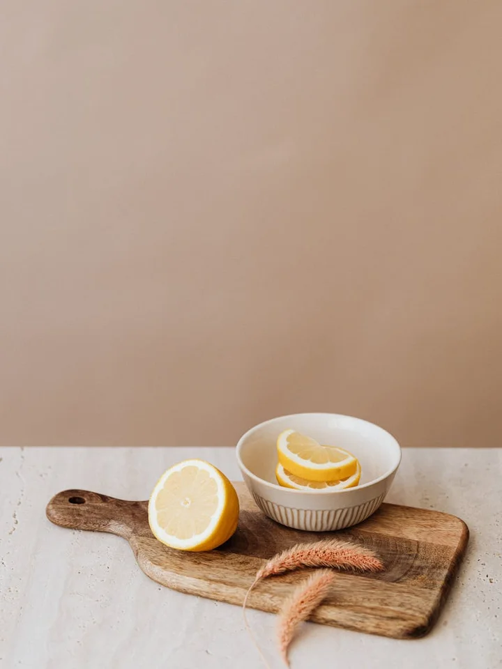 Lemon halves on a wooden cutting board with a small bowl of lemon wedges, illustrating freshness and citrus origin of vitamin C in skincare.