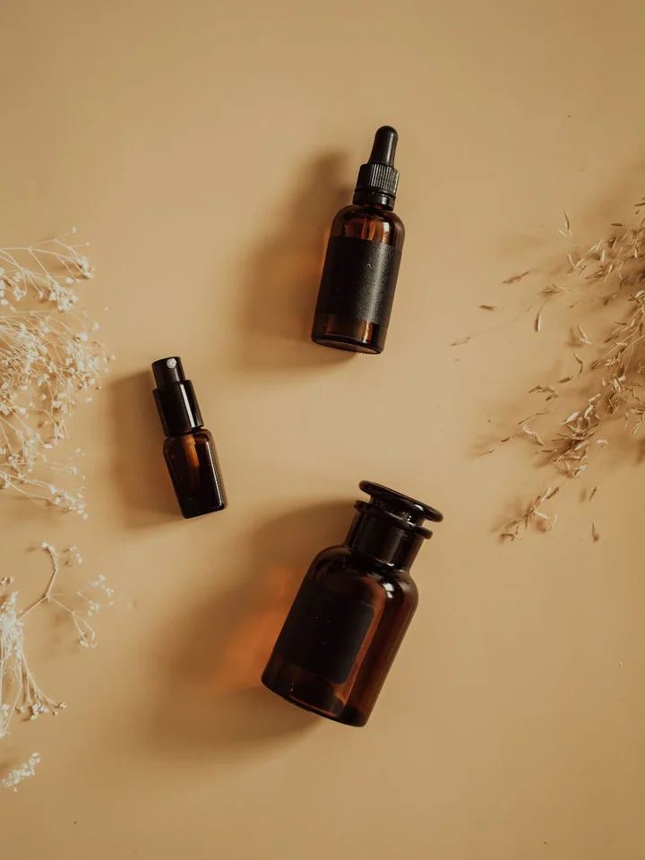 Three amber glass skincare bottles with droppers and a pump on a beige background, arranged to suggest a calm, curated acid skincare routine.