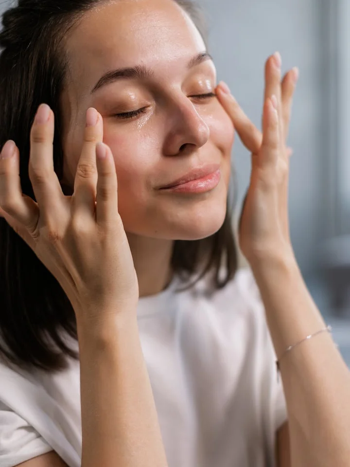 Woman with eyes closed, hands near her face, gently applying skincare.