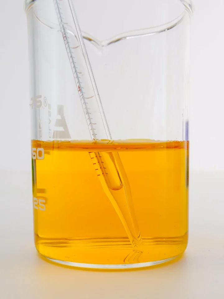 Beaker containing orange glycolic acid solution with a glass pipette resting inside