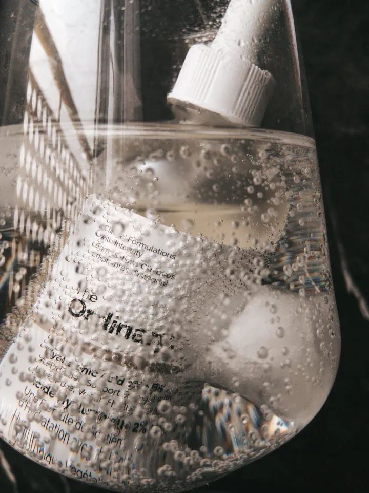 Close-up of a clear bottle with a white cap and bubbles in the liquid, set against a dark background.